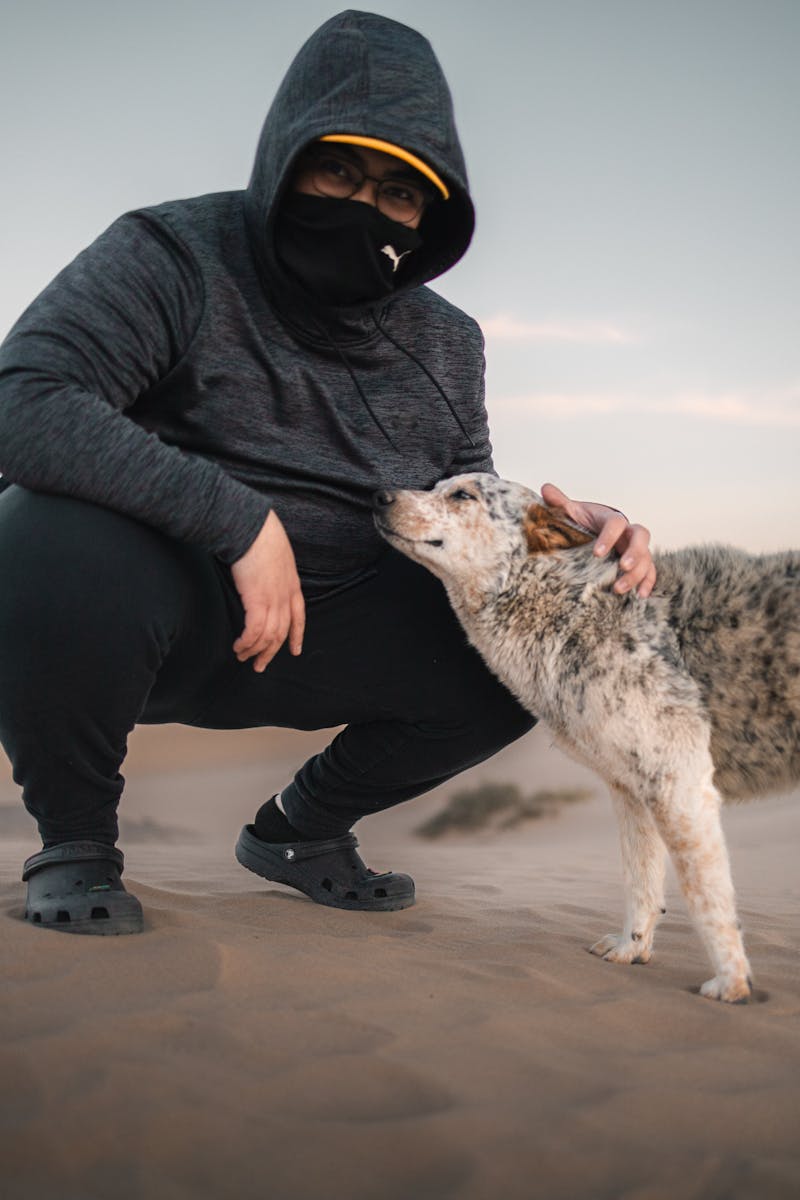 A masked adult with a dog in the sandy dunes of Samalayuca Desert, Mexico.