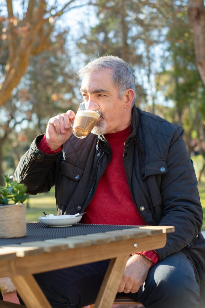 Senior man in black jacket drinking coffee at a park in Portugal. Daylight setting.